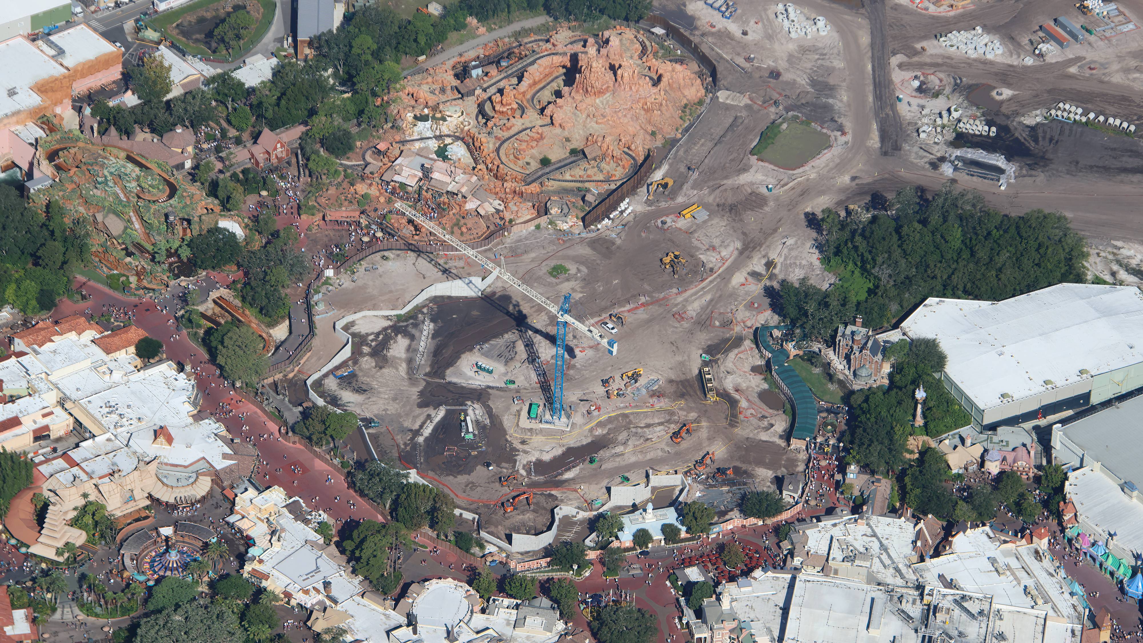 Aerial view of the Piston Peak construction zone with a tower crane, earthwork, and Big Thunder Mountain Railroad