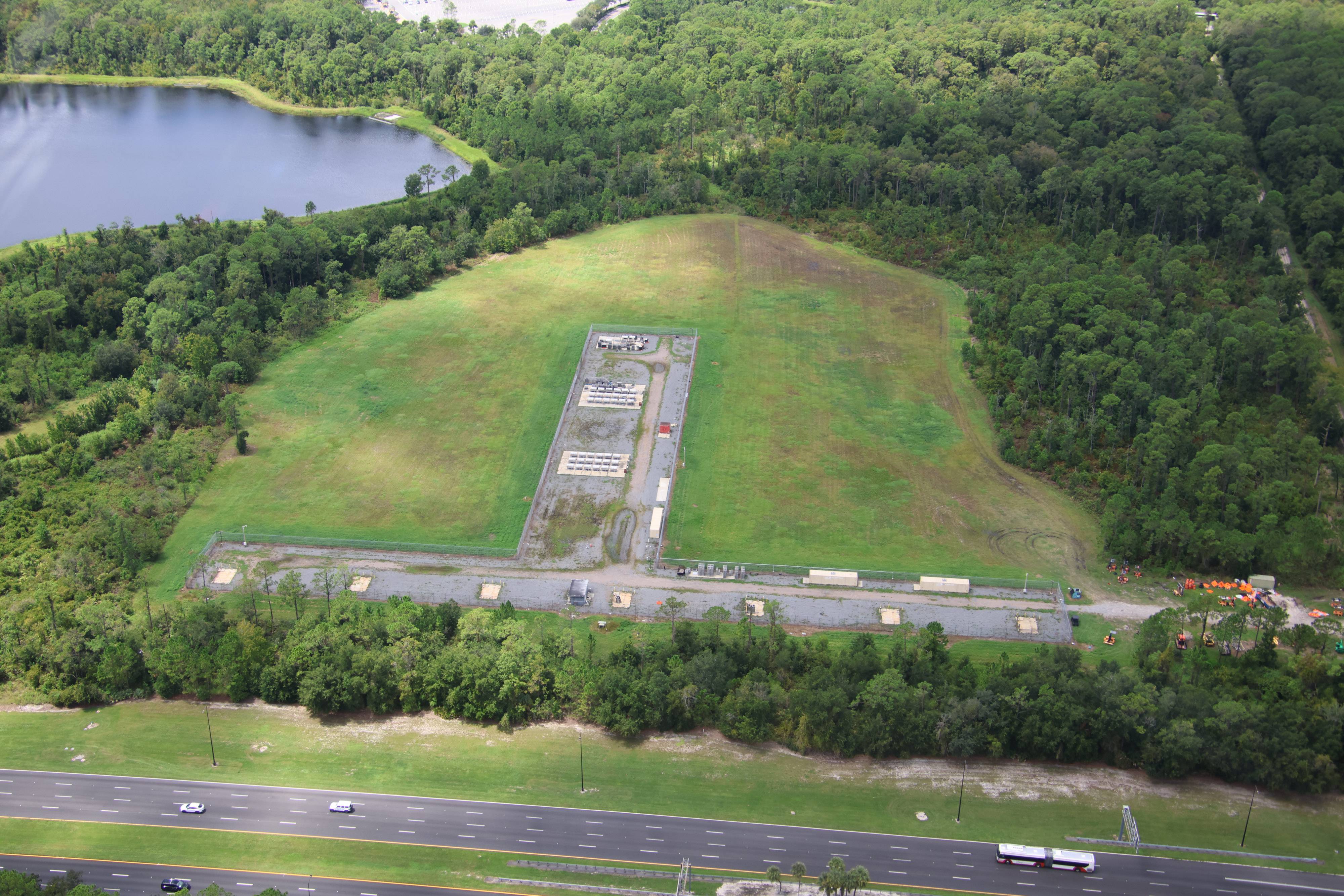 Aerial view of the World Drive fireworks launch site showing the grassed launch area, equipment staging, and access road running parallel to World Drive below