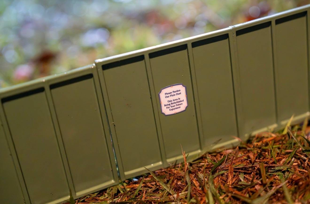 A "Please Pardon Our Pixie Dust" refurbishment sign on a green construction barrier at the Germany pavilion's train garden