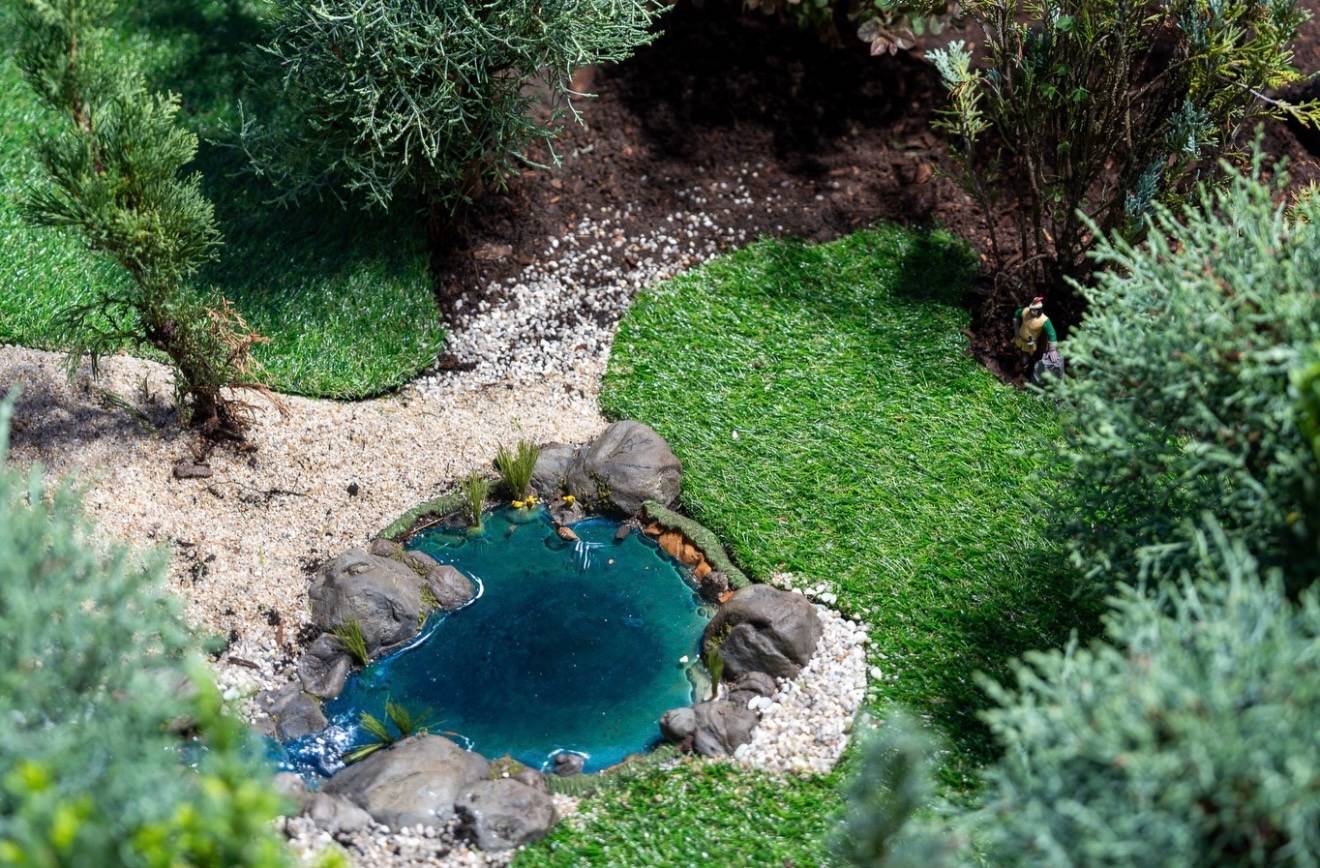 Miniature pond with rocks, gravel, and a small gardener figure nestled among detailed landscaping in the Germany pavilion train garden