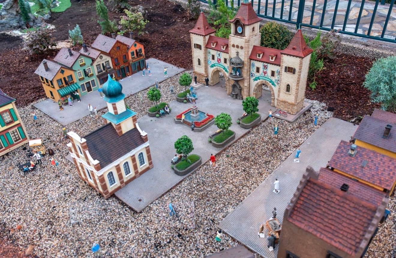 Aerial view of the Germany pavilion train garden showing miniature Bavarian buildings, a central fountain plaza, and an arched gateway tower with clock and red spire rooftops