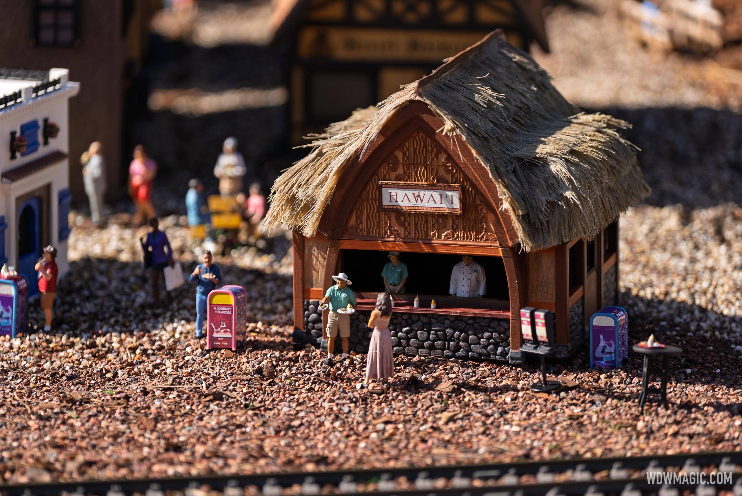 The Hawaii booth miniature in the Germany pavilion train garden features tiny figures at the counter beneath a thatched roof with carved wooden detailing