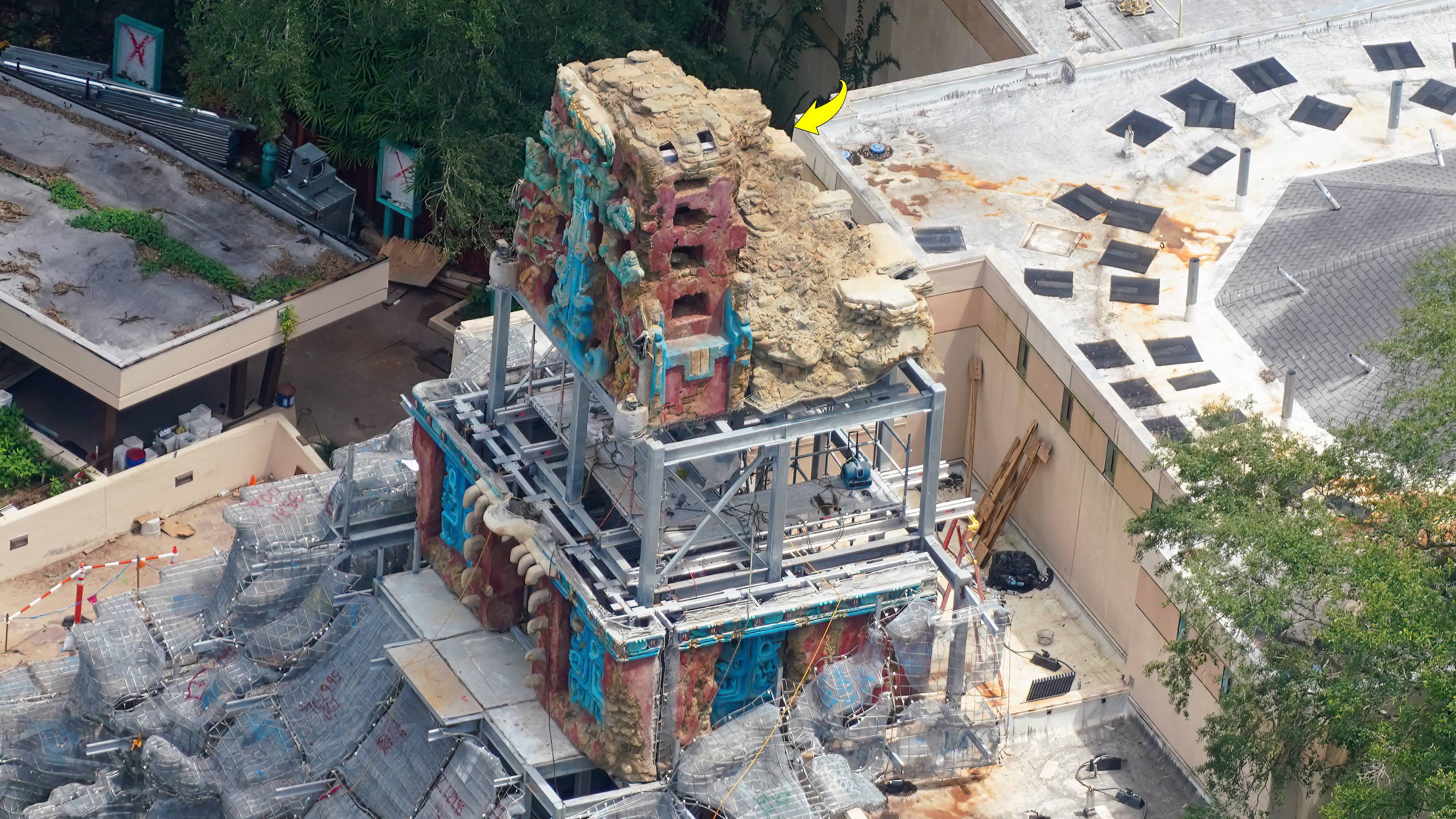Scaffolding surrounds the partially completed temple facade tower, with detailed Maya-inspired carvings and turquoise accents visible from above