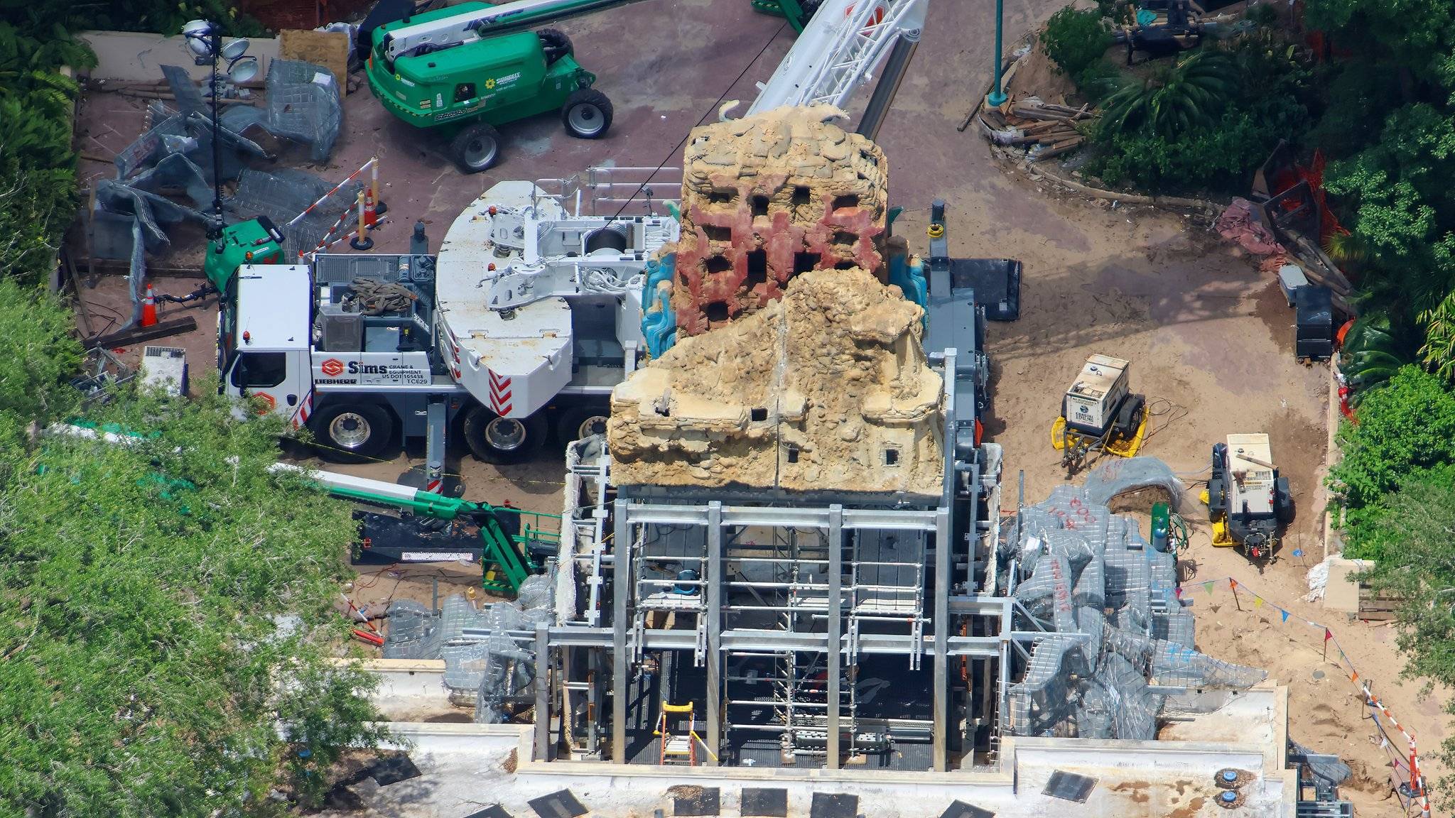 A crane sits alongside the installed temple facade sections, with detailed stone carvings and red hieroglyph-style markings visible from above