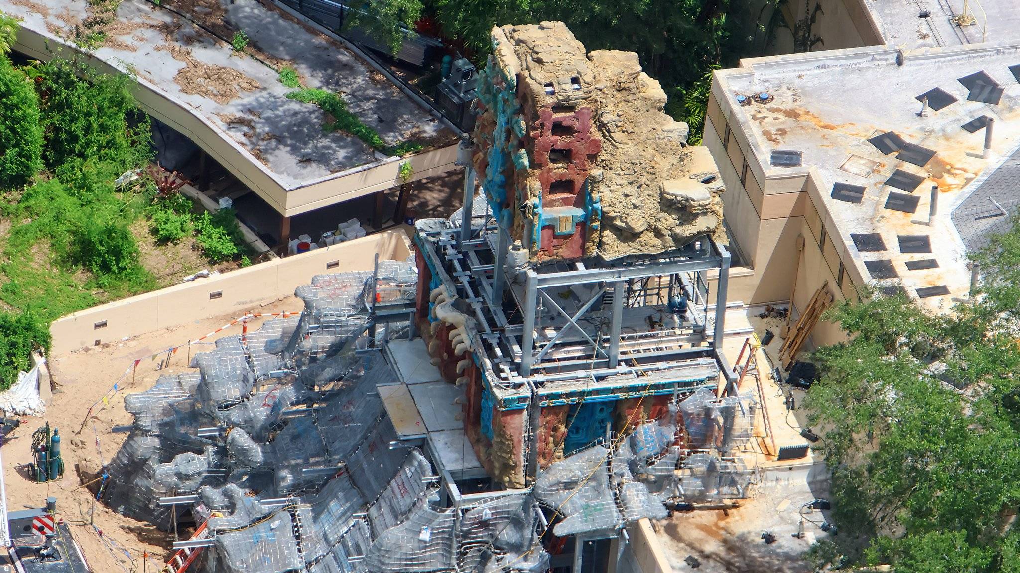Steel support framework and scaffolding surround the rising temple facade tower, with turquoise and red Maya-inspired carvings visible mid-construction