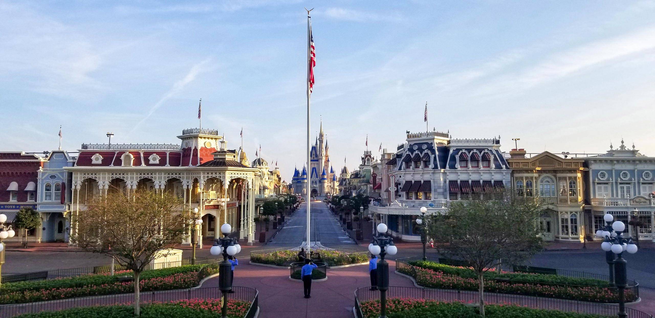 Security Cast Members raise the flag at a closed Magic Kingdom due to COVID-19
