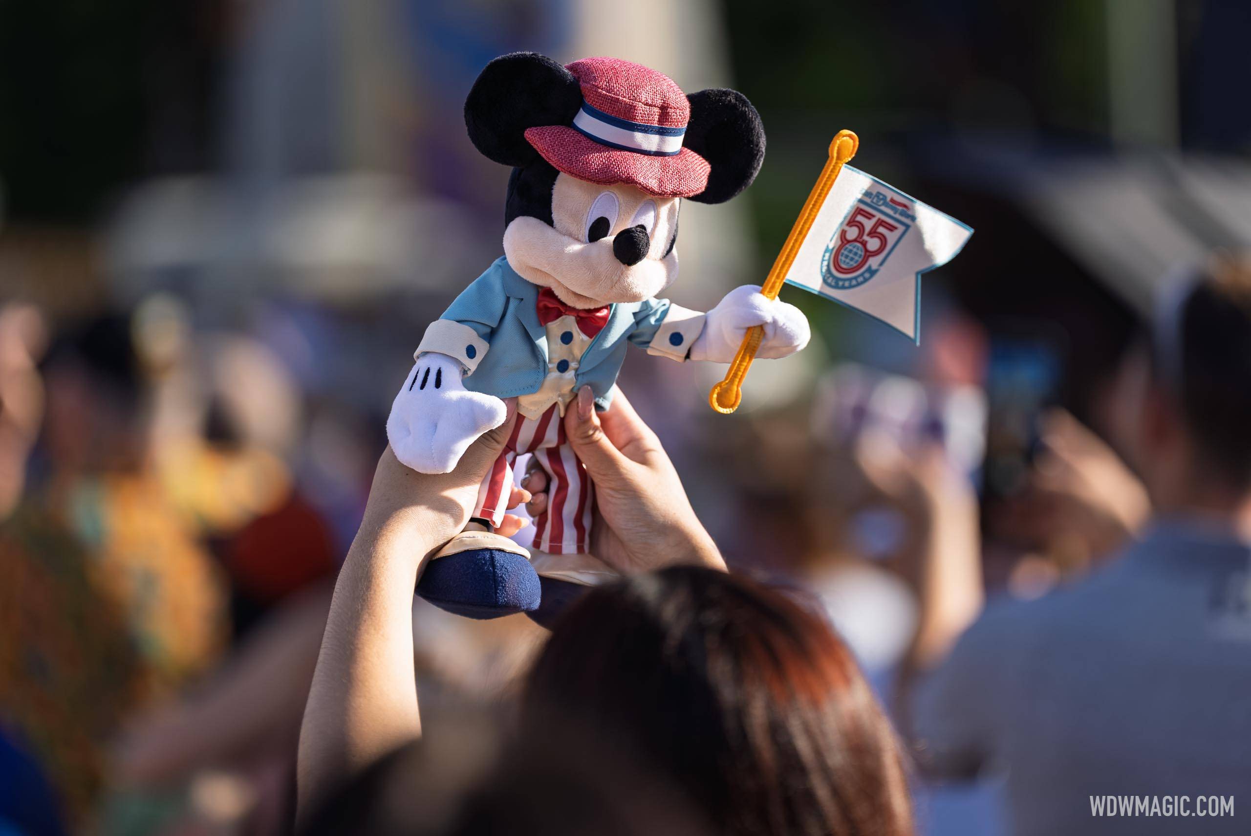 A guest holds up a Mickey Mouse 55th anniversary plush above the crowd gathered in front of Cinderella Castle for the Walt Disney World 55th anniversary celebration