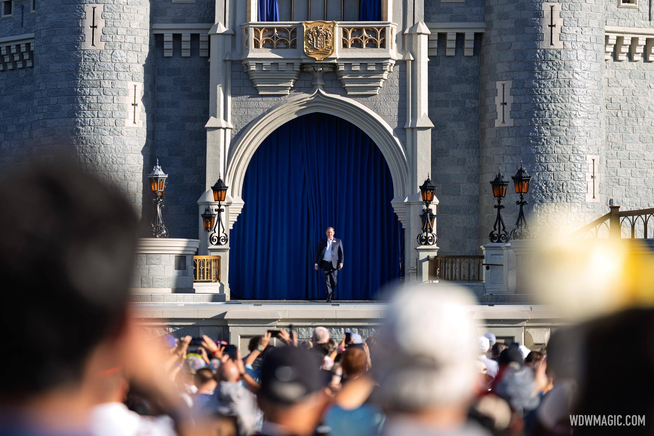 Joe Schott walks out onto the Cinderella Castle stage in front of a large crowd gathered in the hub for the Walt Disney World 55th anniversary celebration