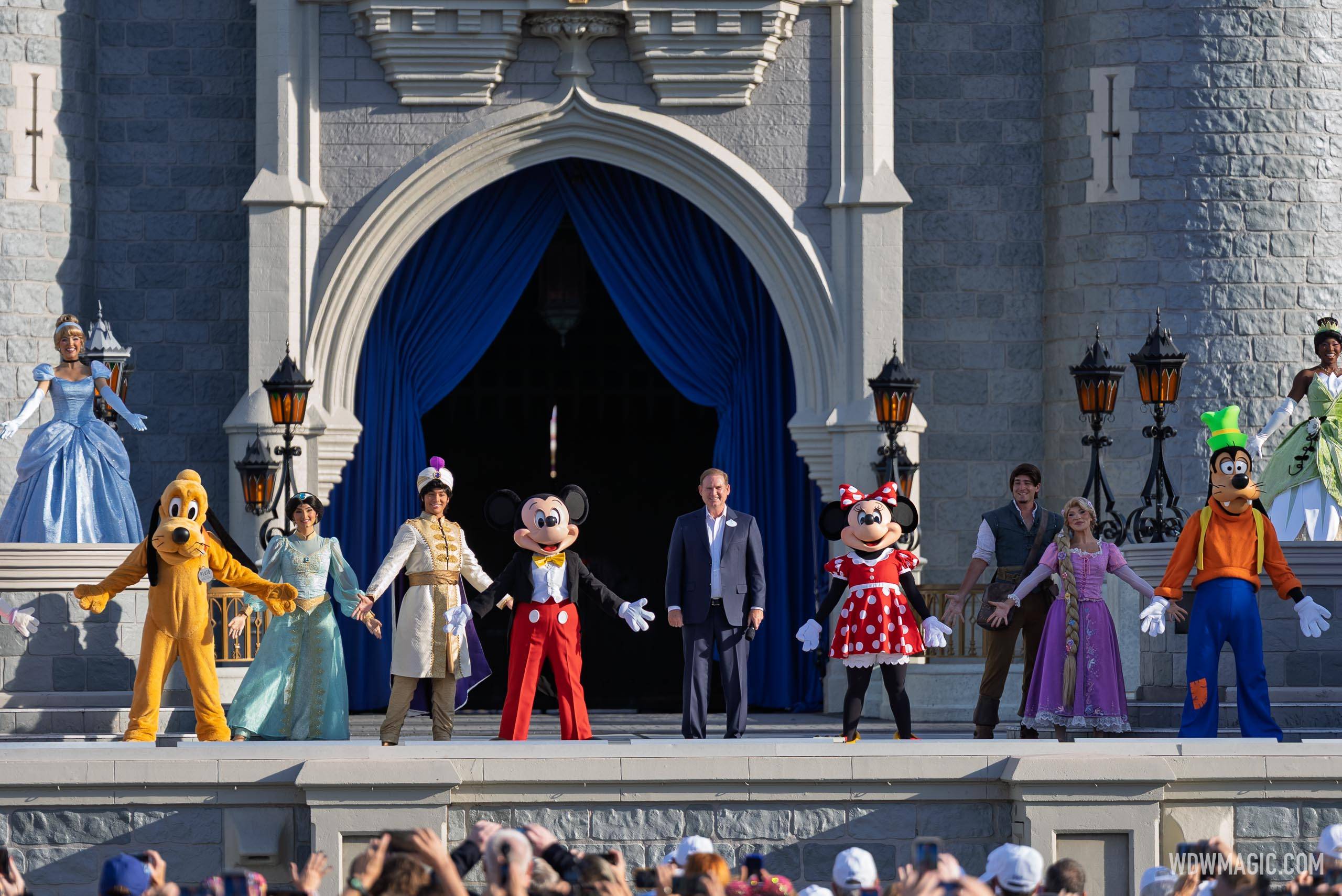 Joe Schott stands with Mickey, Minnie, Goofy, Pluto, and Disney princes and princesses including Cinderella, Tiana, Rapunzel, Jasmine, and Aladdin on the Cinderella Castle stage for the 55th anniversary celebration