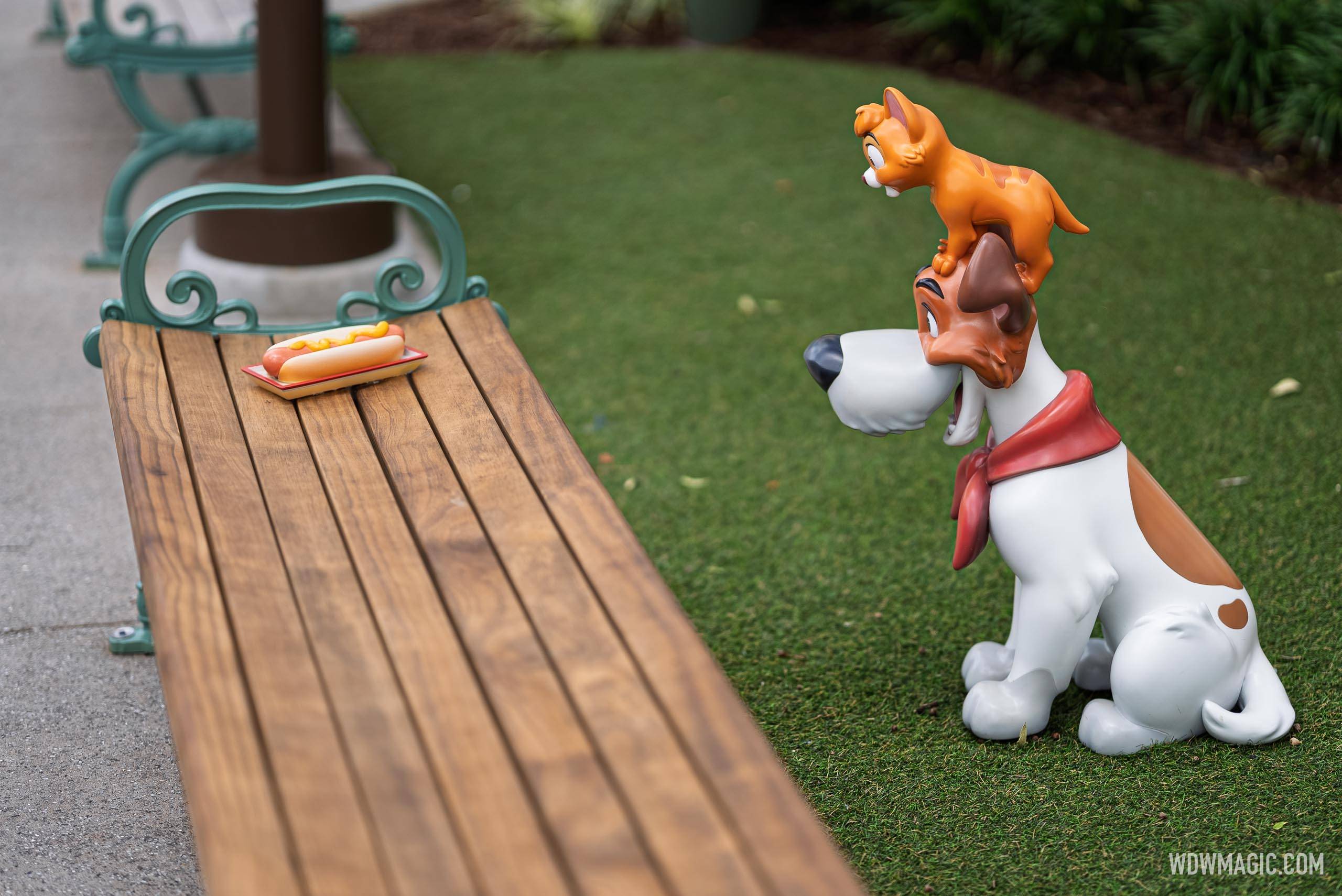 Dodger and Oliver from Oliver & Company eye a hot dog on a nearby park bench in the Walt Disney Studios courtyard