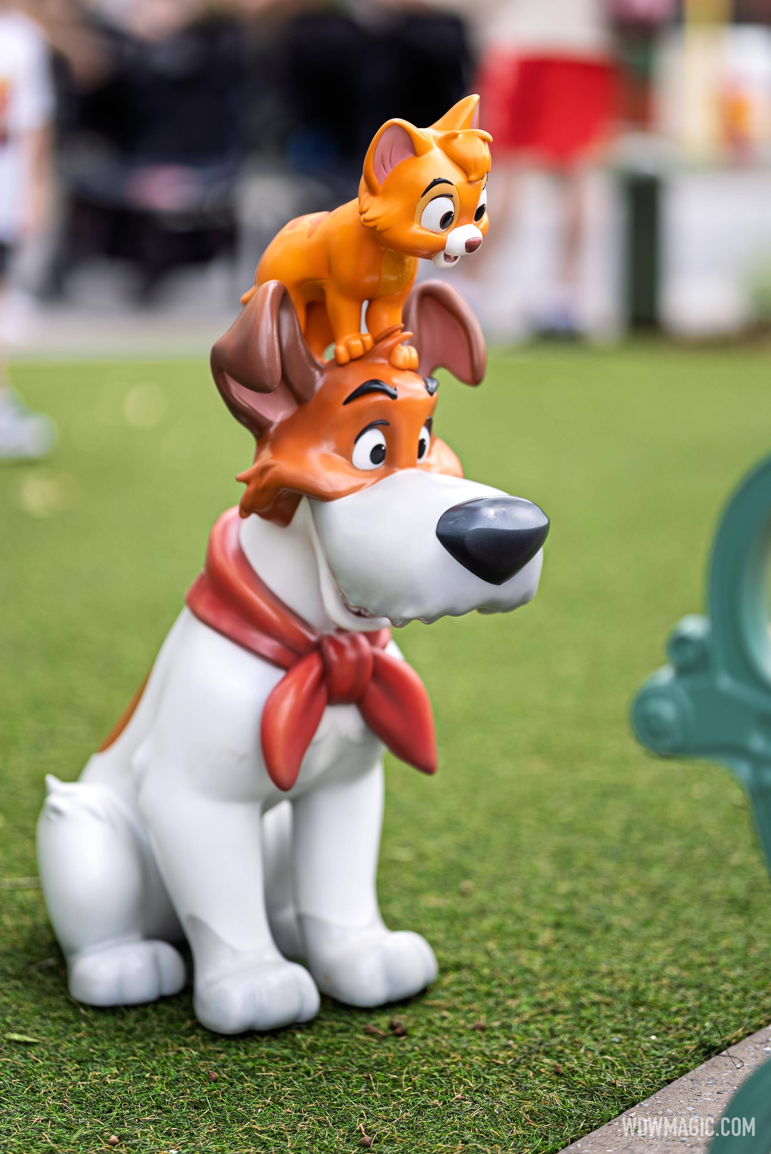 Dodger and Oliver from Oliver & Company sit near a park bench in the Walt Disney Studios courtyard outside The Magic of Disney Animation
