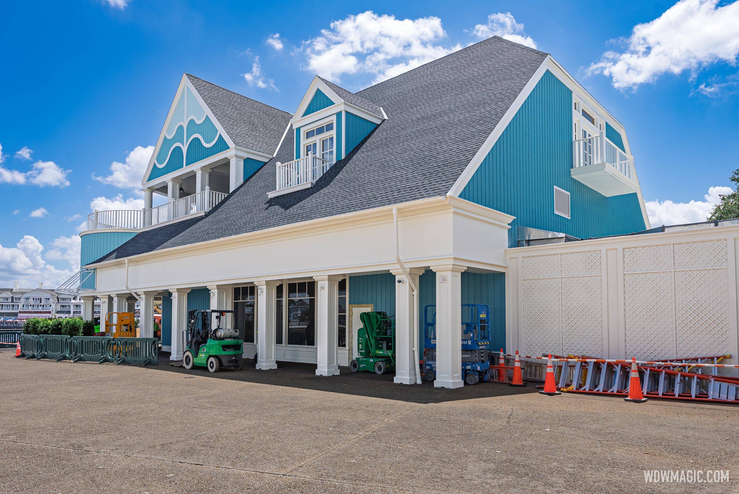 Forklifts and scissor lifts are staged beneath the covered promenade walkway of the teal Hurly-Burly building
