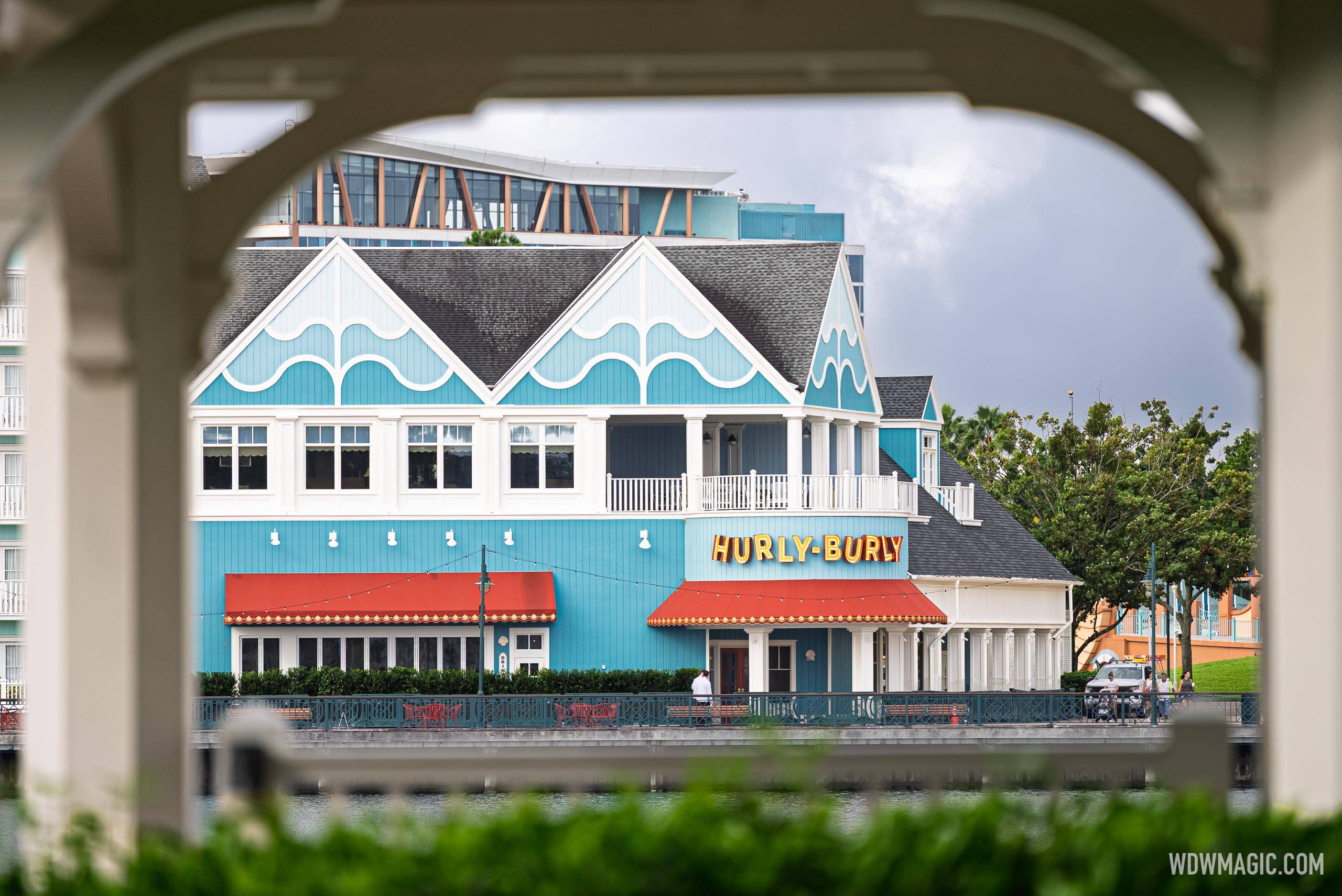 Hurly-Burly's teal wave-themed exterior and lit marquee sign are seen framed through a BoardWalk gazebo arch