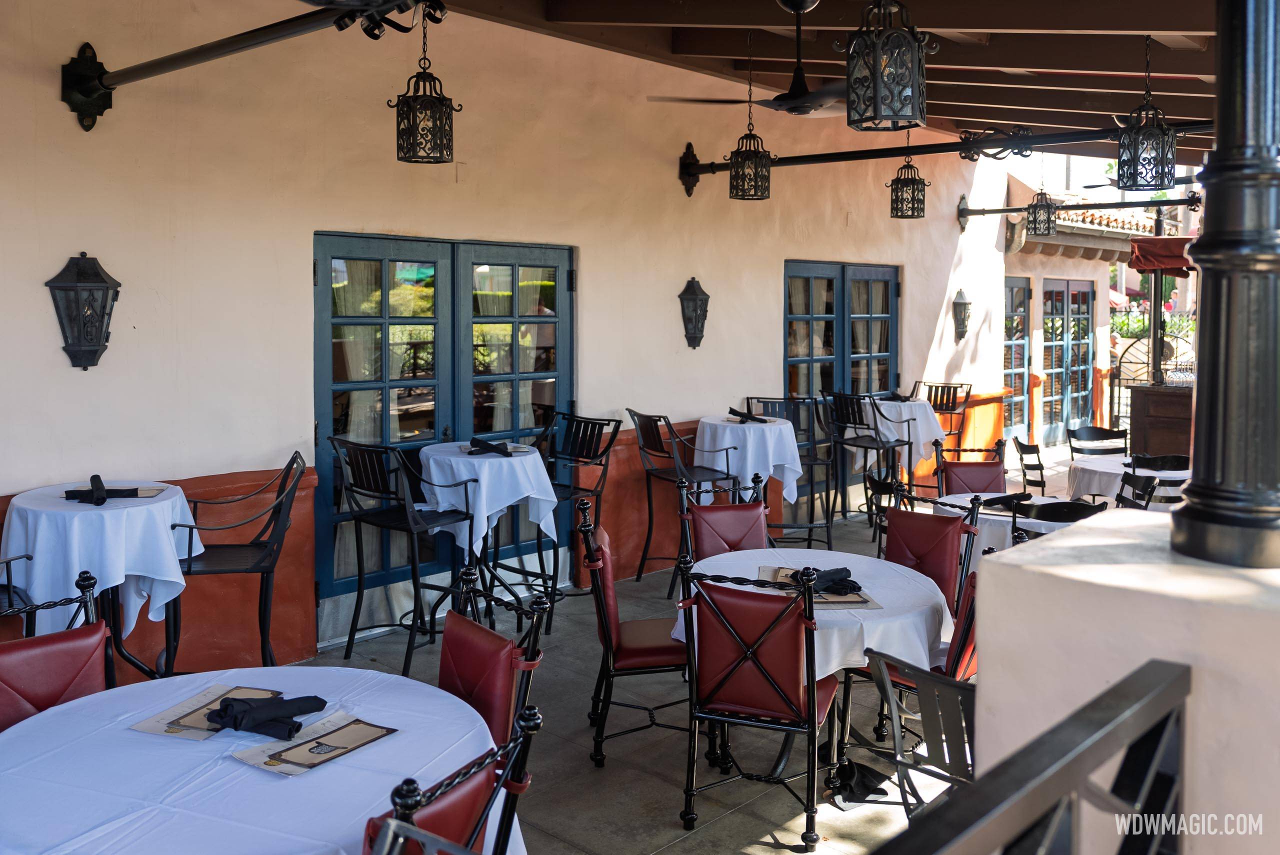 The outdoor lounge seating area features white-clothed tables, red and black iron chairs, wrought iron pendant lanterns, and ceiling fans beneath the new permanent canopy