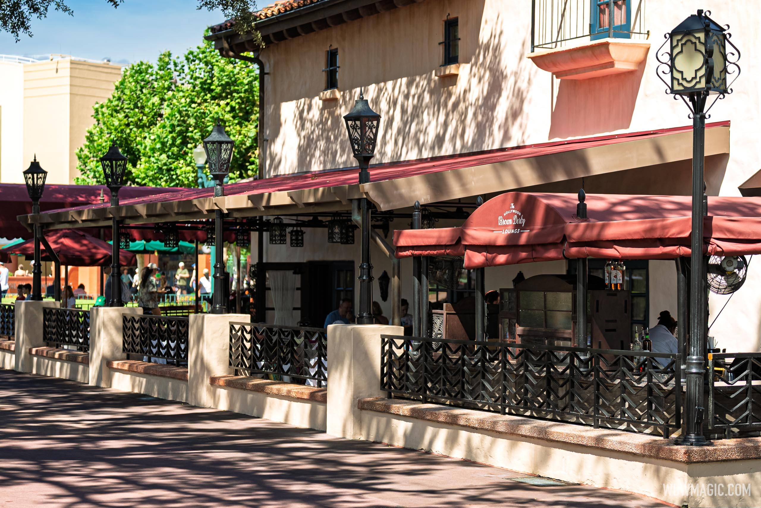 The Hollywood Brown Derby Lounge exterior shows the refurbished patio with its new permanent red canopy, updated black lantern-style light poles, and decorative wrought iron fencing along the walkway
