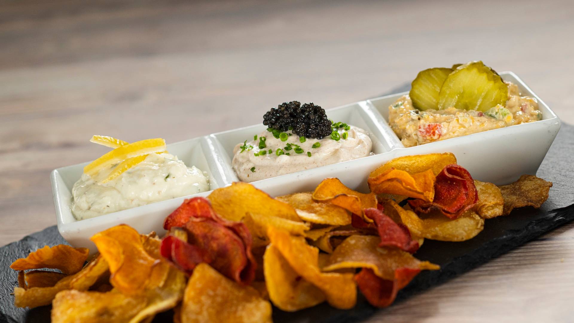 Trio of Dips and Chips: House-made potato chips with whipped feta dip and candied lemon, caramelized onion dip and caviar, and pimento cheese and pickles