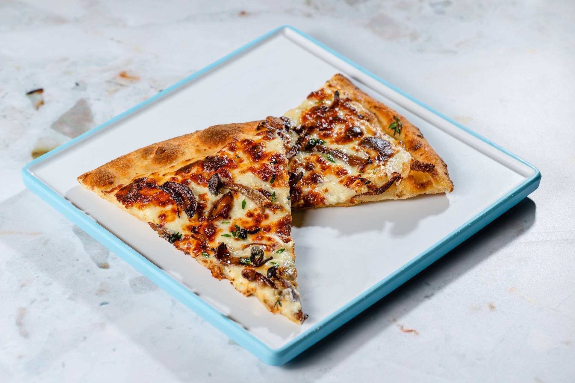 Pizza Bianca: Two slices of freshly baked pizza topped with roasted wild mushrooms, garlic cream, mozzarella, cheese blend, truffle oil, and thyme (New)