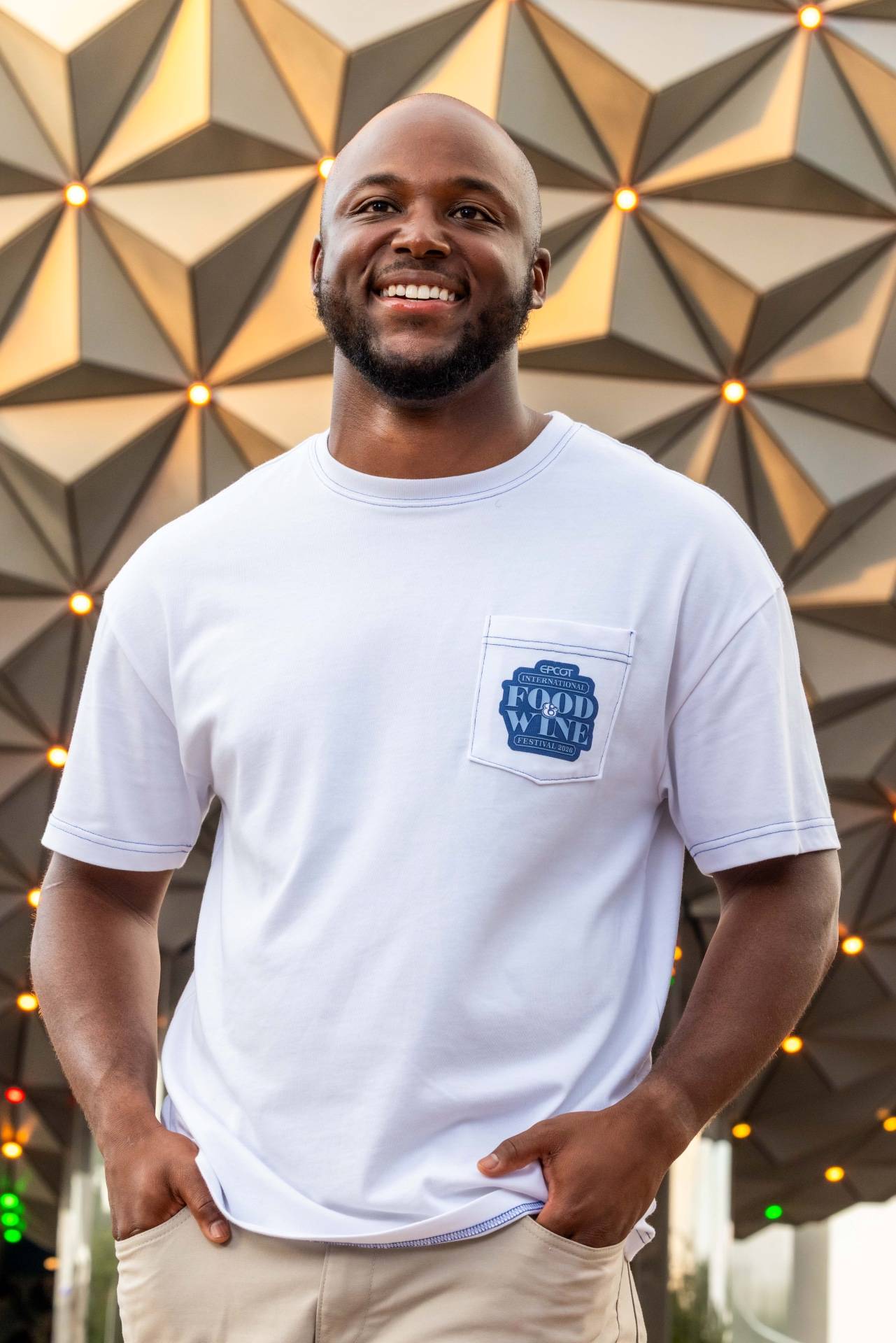 White EPCOT International Food & Wine Festival 2026 pocket tee modeled by a man smiling in front of Spaceship Earth