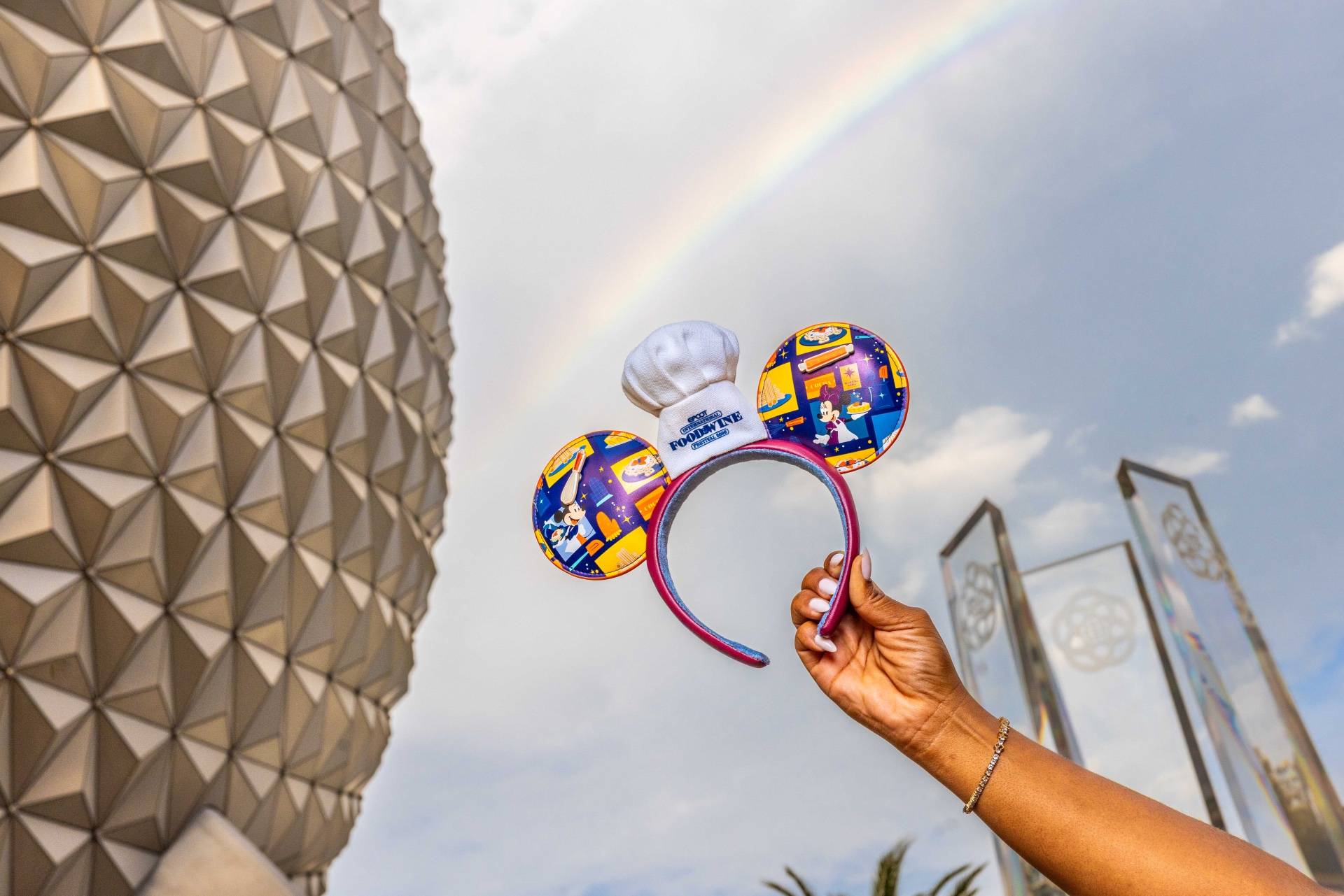 Chef-themed Mickey ears headband from the 2026 EPCOT International Food & Wine Festival collection held up in front of Spaceship Earth