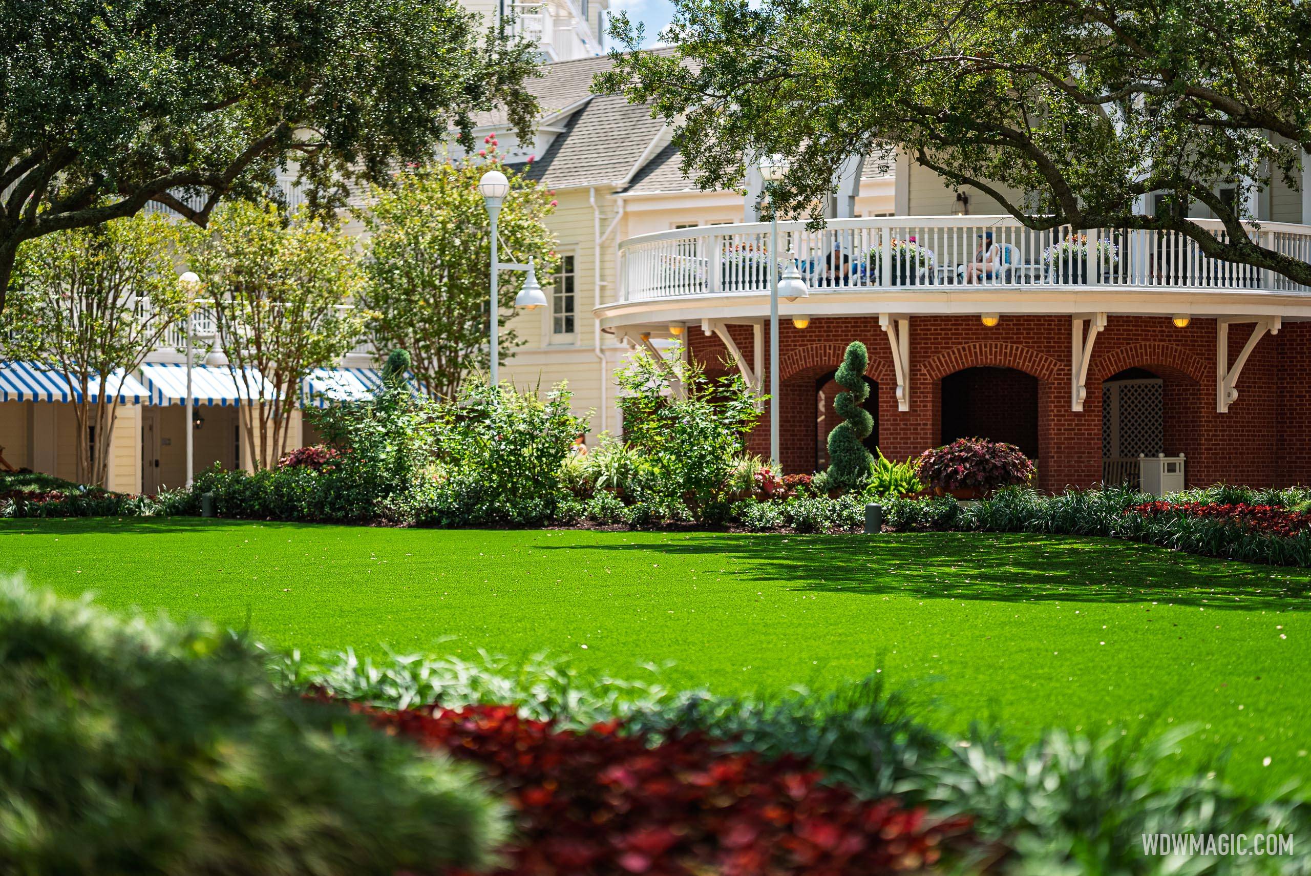 Lush artificial turf stretches across the Village Green courtyard, with the BoardWalk Inn's brick rotunda and upper balcony visible beyond the manicured gardens
