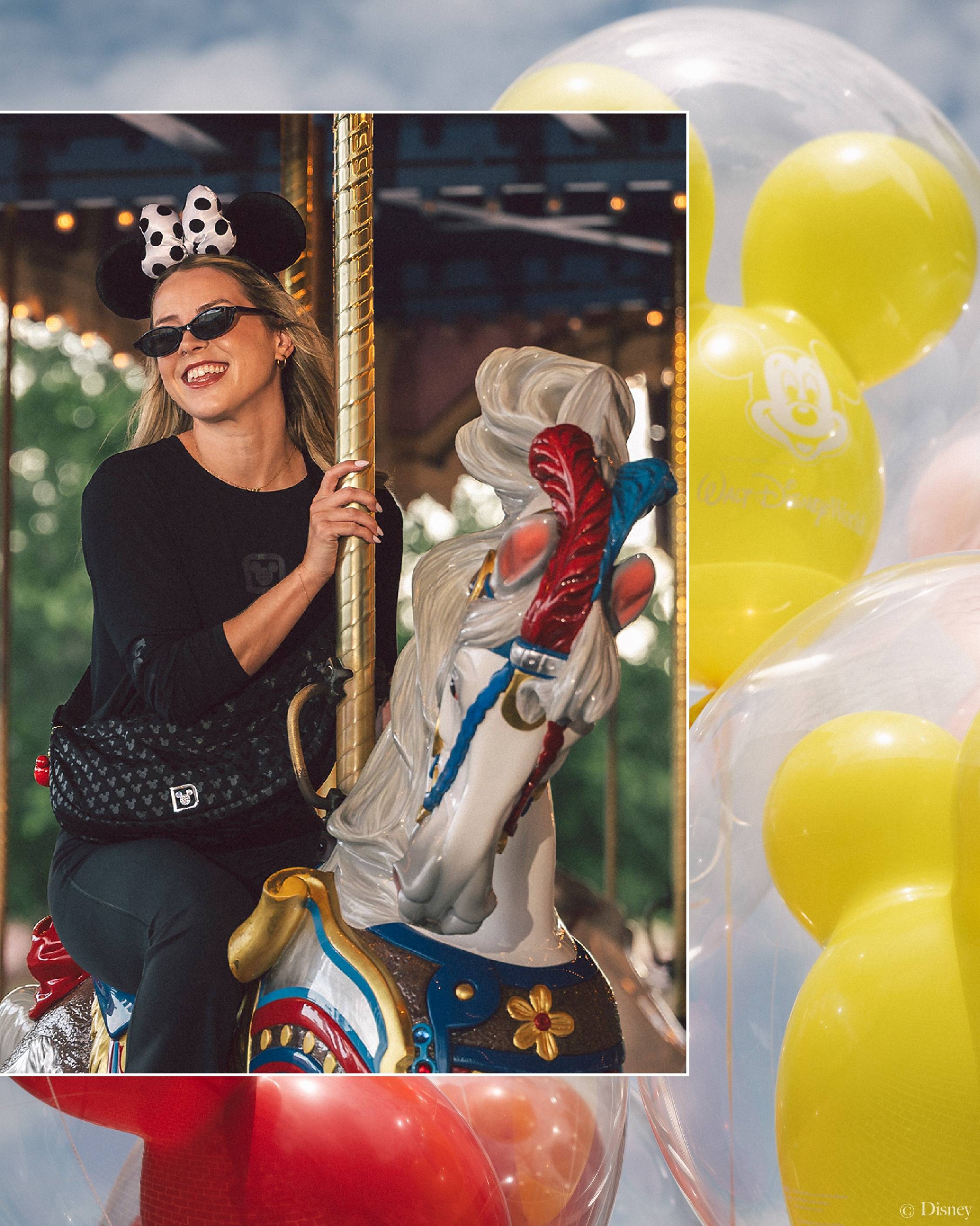 A model wears the Midnight Magic color story while riding Prince Charming Regal Carrousel, styled with a black long-sleeve top, fanny pack, and Minnie ears