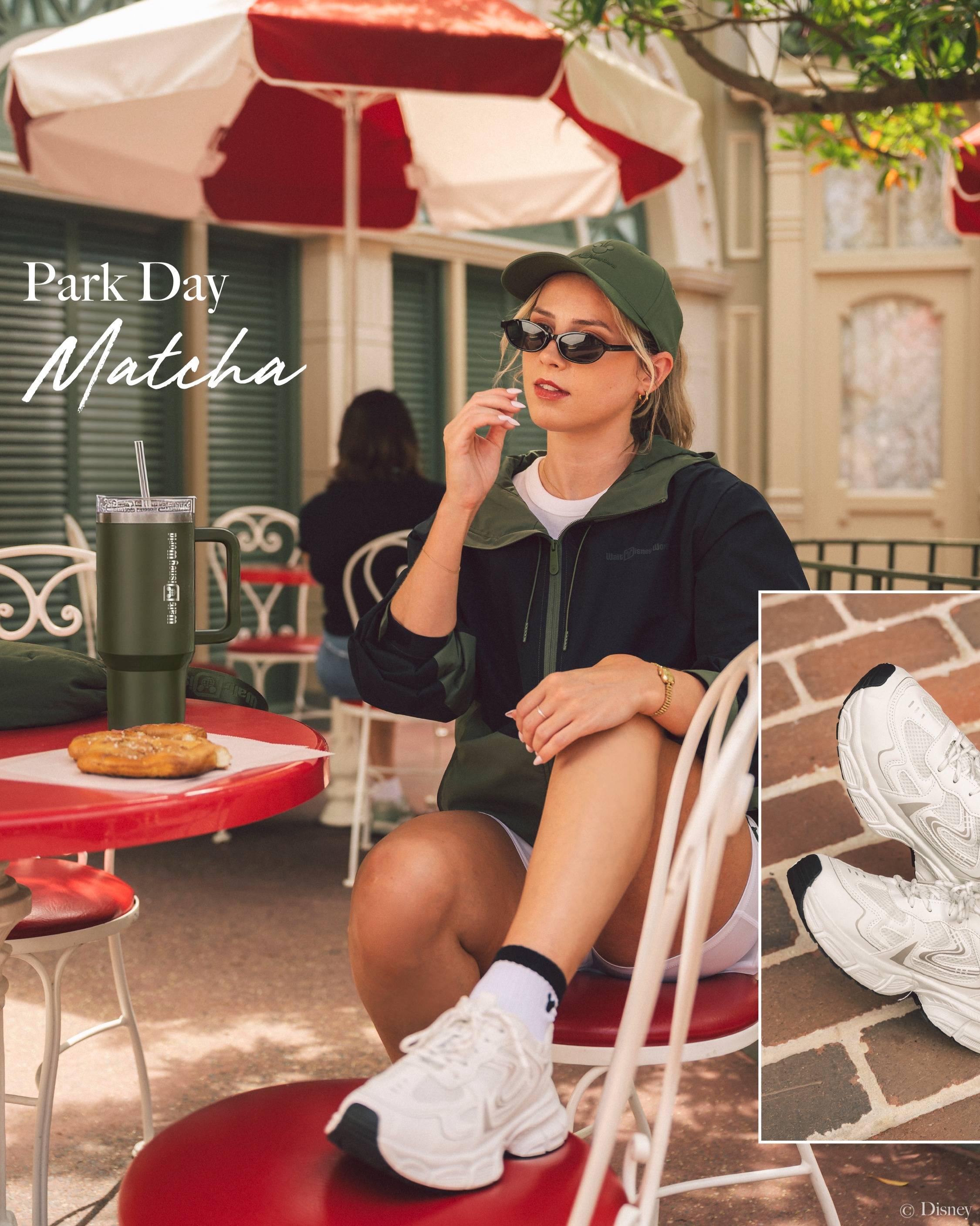 A model wears the Park Day Matcha color story from the new Walt Disney World athleisure collection, including a black and green zip hoodie, white shorts, and green cap, alongside a matching Walt Disney World tumbler