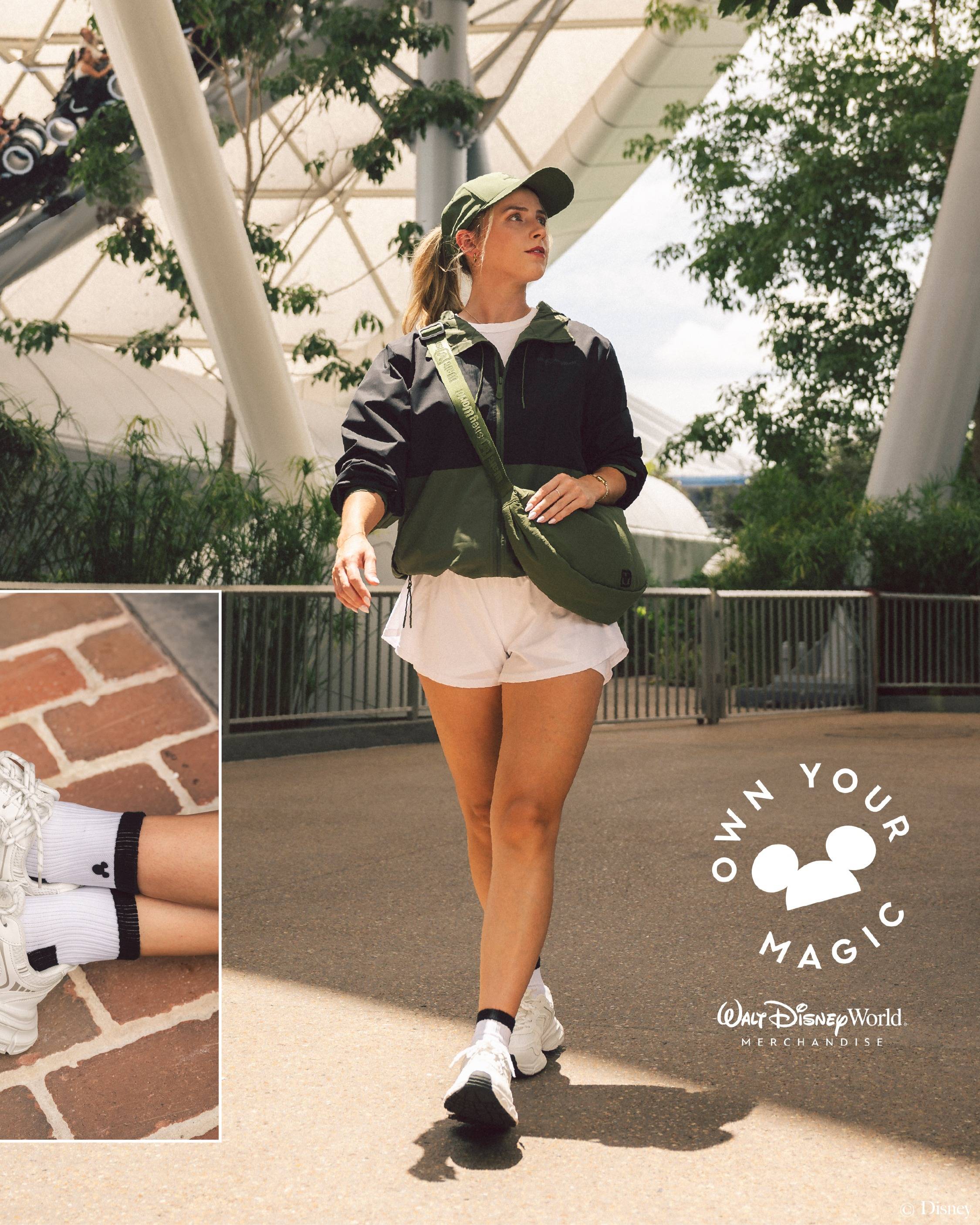 A model wears the Park Day Matcha color story at EPCOT, styled with a black and green zip hoodie, white shorts, green cap, and olive crescent bag, with a detail shot of Mickey-embroidered socks