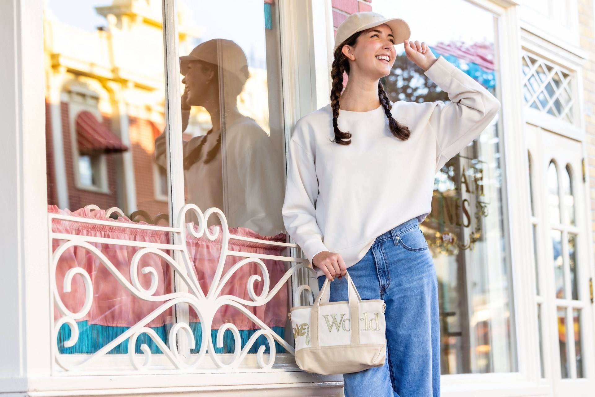 A model carries the cream and gold Walt Disney World Logo Mania tote bag in the Storybook Soft Serve colorway